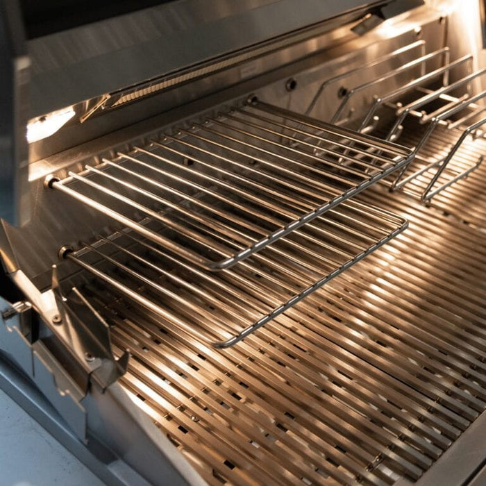 Stainless steel grill interior showing main cooking grates and adjustable warming rack under built-in lights.
