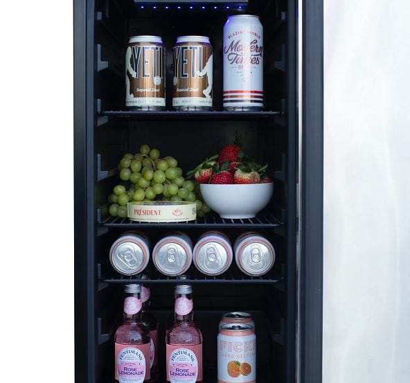 Refrigerator interior stocked with cans, bottles, grapes, strawberries in a bowl, and assorted beverages on adjustable shelves.