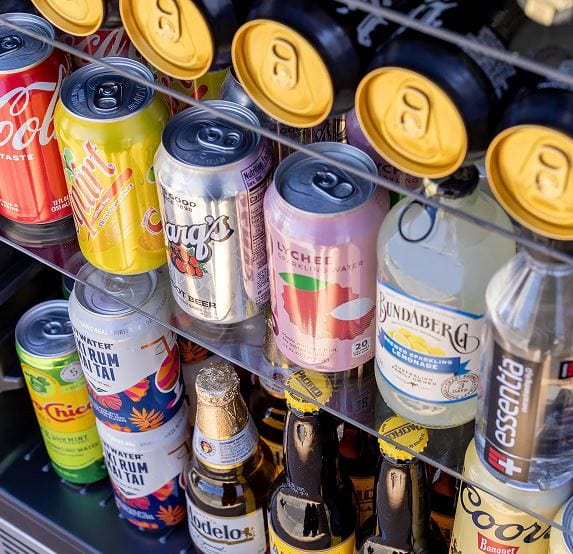 Close-up of a stocked beverage fridge featuring various cans and bottles arranged on glass shelves for easy access and visibility.