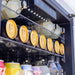 Close-up of a beverage fridge interior, showcasing neatly stacked cans, bottles, and illuminated shelves under LED lighting.