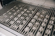 Close-up of a stainless steel grill interior showing thick grill grates and ceramic briquettes arranged underneath for heat distribution.