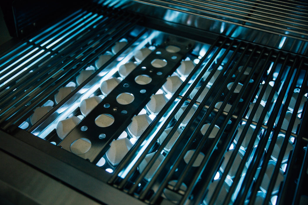 Stainless steel gas grill with ceramic briquettes and visible blue flames, evenly heating for efficient cooking performance.