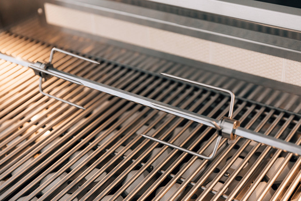 Close-up of a stainless steel grill with a rotisserie rod and meat forks positioned over the grill grates.