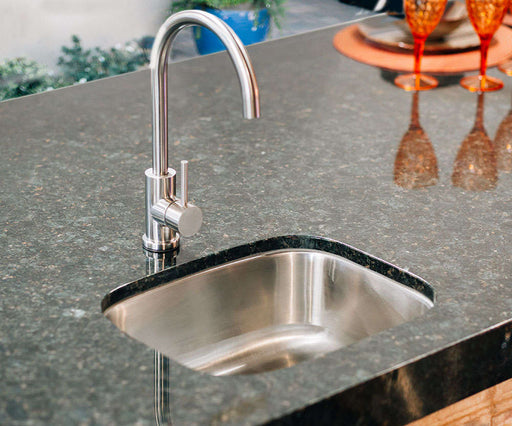 A stainless steel undermount sink with a modern high-arc faucet, installed in a polished granite countertop with elegant decor nearby.