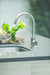 A stainless steel undermount sink with a modern high-arc faucet, installed in a sleek countertop, accented with fresh greenery decor.