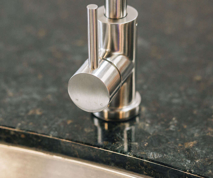 Close-up of a stainless steel faucet handle on a polished granite countertop, with hot and cold indicators engraved on the control knob.