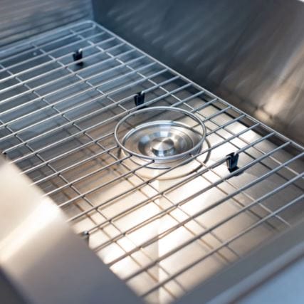 Close-up of a stainless steel sink with a protective grid, showcasing a polished circular drain and angular basin design for efficient water flow.