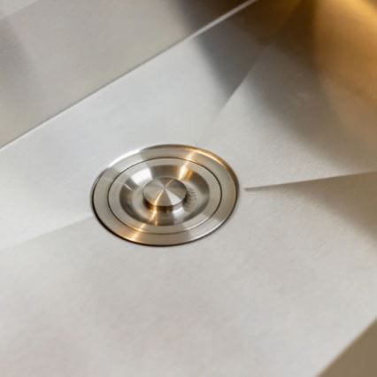 Close-up of a stainless steel sink bottom featuring a modern circular drain with a sleek, polished design and angular basin slopes.