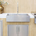 A modern stainless steel apron-front sink with a sleek faucet, installed in a white countertop and complemented by bamboo wall decor.