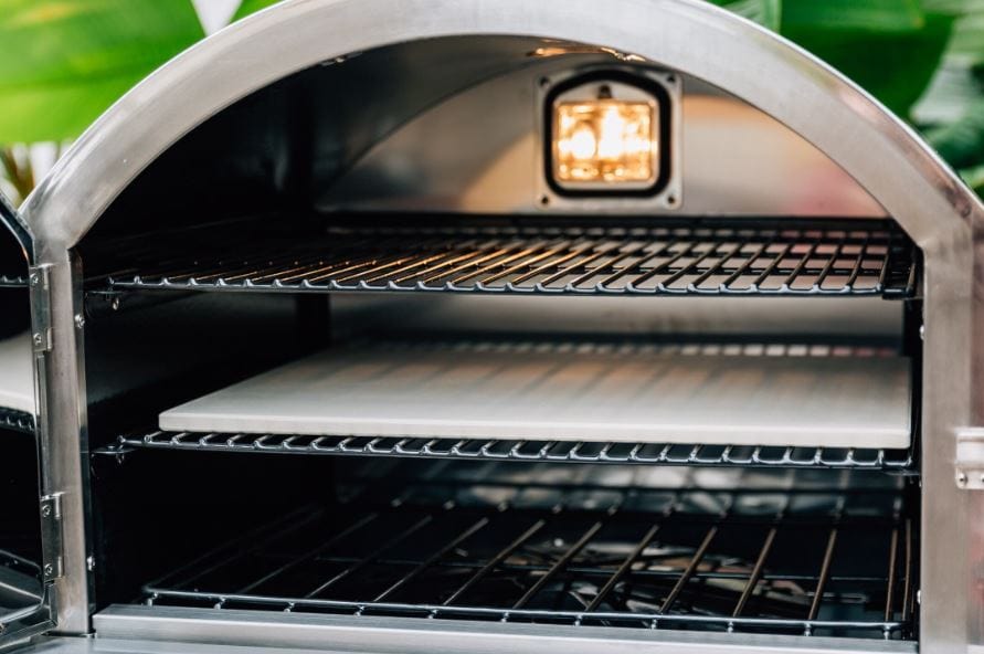 Interior of a stainless steel pizza oven featuring multiple racks, a cooking stone, and an illuminated light for visibility.