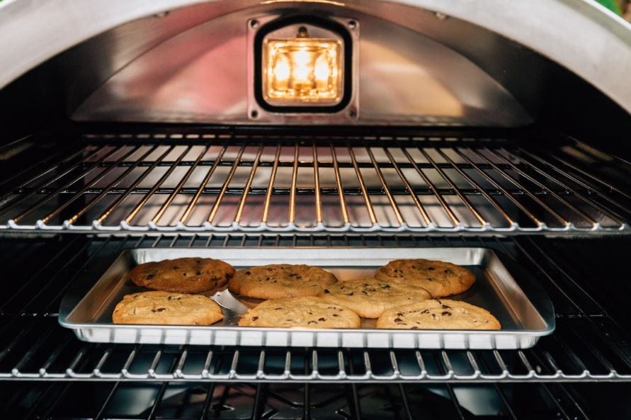 Interior of an oven with a tray of freshly baked cookies on the middle rack, illuminated by a light, showcasing clean steel racks.