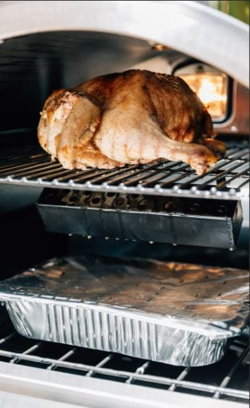 Interior of an oven with a roasted chicken on the upper rack, a smoker box beneath, and a foil-covered tray on the bottom rack.