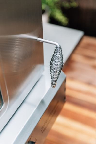 Close-up of a heat-resistant coiled handle attached to a stainless steel oven door, with wooden decking visible in the background.