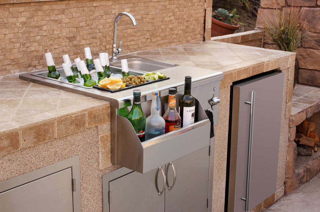 An outdoor bar station with a sink, faucet, storage compartments, beverage bottles, ice, garnishes, and a built-in stone countertop.