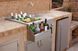 An outdoor bar station with a sink, faucet, storage compartments, beverage bottles, ice, garnishes, and a built-in stone countertop.