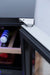 Close-up of a metallic hinge on the door frame of a cooler, showing bottles and wooden racks inside, with a sleek black finish.