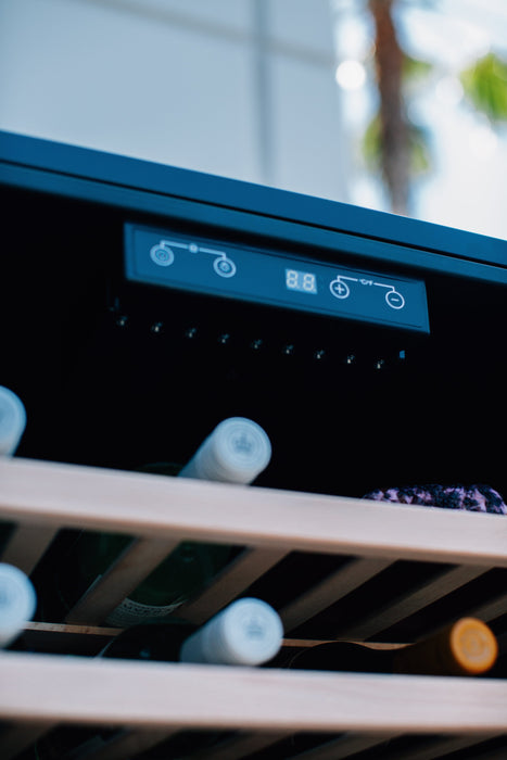 Close-up of a cooler's control panel, shelves, and stored wine bottles, with an outdoor background visible through reflections.