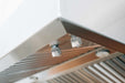 A close-up view of a vent hood's underside, showcasing stainless steel finish, control knobs, and vented panels for efficient airflow.