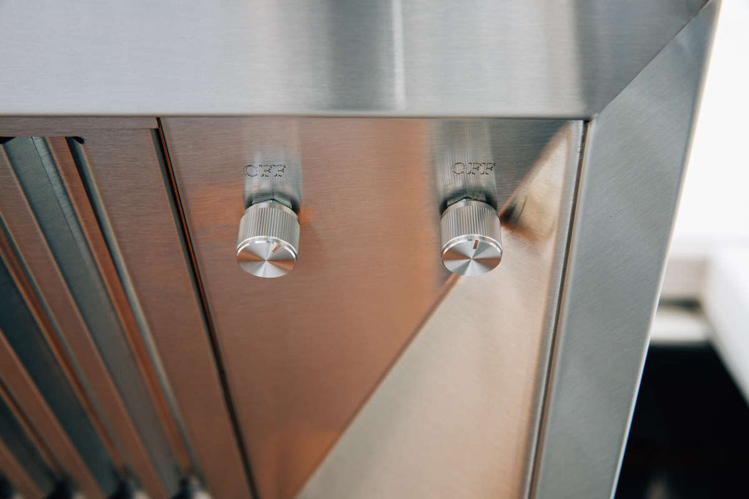 A close-up of a stainless steel vent hood showing two control knobs and slatted vent panels, designed for efficient kitchen ventilation.