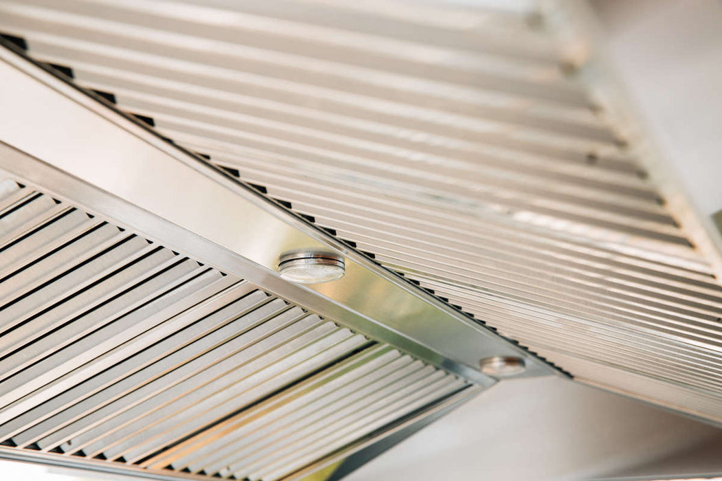 A close-up view of the underside of a vent hood, showing stainless steel slatted filters and a smooth metallic finish for ventilation.