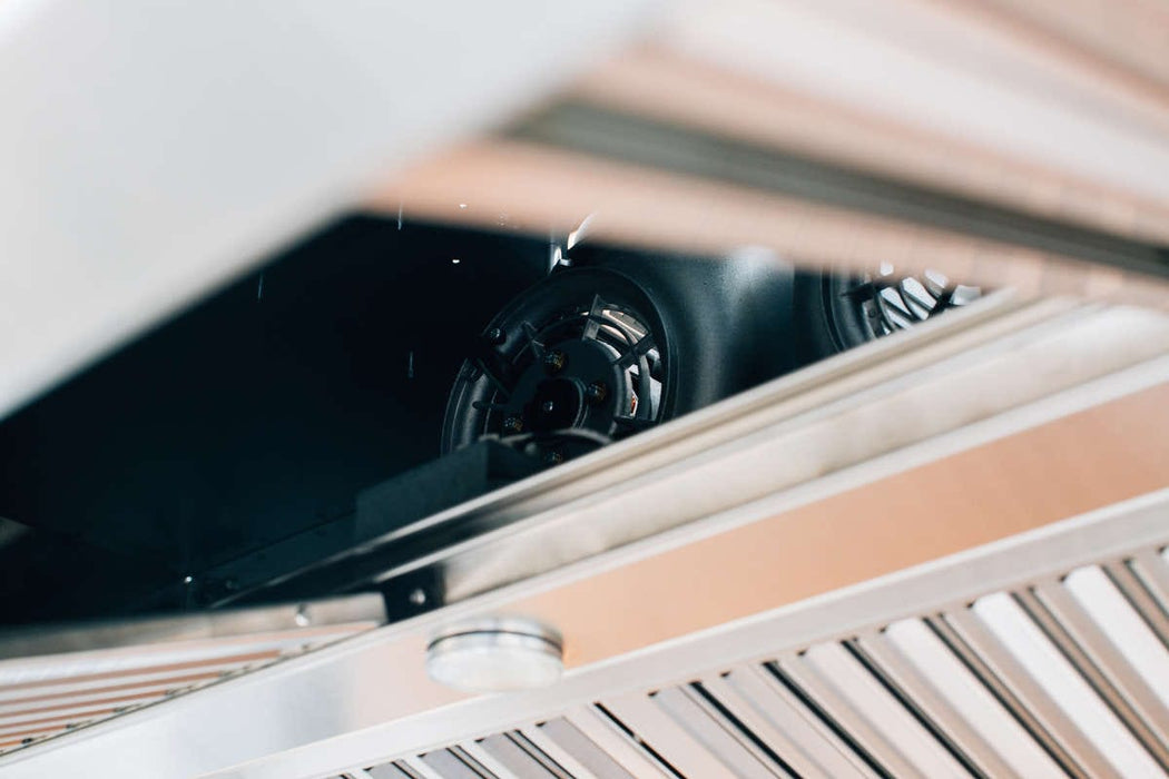 A detailed view of the interior components of a vent hood, showing the fan mechanism, stainless steel slatted filters, and a light fixture.