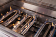 Close-up of lit stainless steel U-shaped burners in a gas grill with visible blue flames and reflective surfaces.