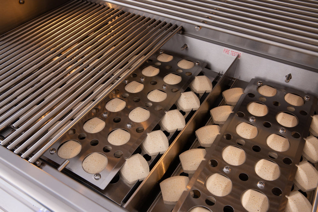 Close-up of a grill interior showing stainless steel grates and ceramic briquettes evenly placed in metal trays for heat distribution.