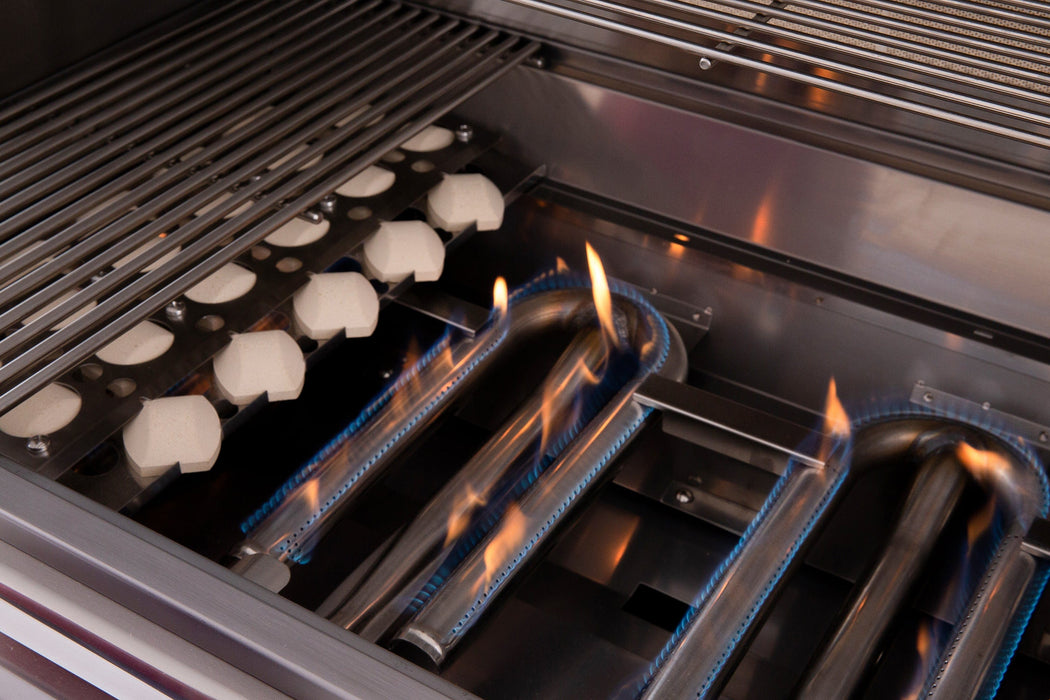 Close-up of an open gas grill showing blue flames on stainless steel burners and ceramic briquettes under grill grates.