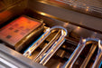 Close-up of a gas grill interior featuring glowing red infrared heat emitter and stainless steel tube burners with visible blue flames.