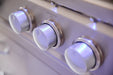 Close-up view of illuminated stainless steel control knobs on a gas grill, showing precise controls and modern blue lighting accents.