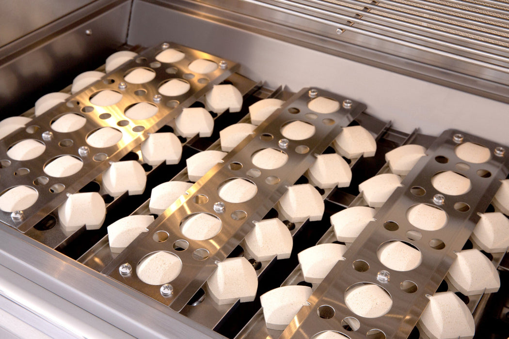 Close-up of a grill interior with ceramic briquettes neatly arranged in stainless steel trays, designed for even heat distribution.