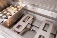 Close-up of a grill interior showing stainless steel burner components, ceramic briquettes, and trays designed for heat distribution.