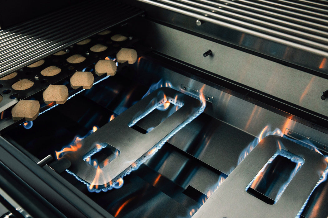 Close-up of an ignited grill interior showing blue flames on stainless steel burners with ceramic briquettes for even heat distribution.