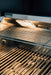 Close-up of an illuminated stainless steel grill interior featuring clean grilling grates, warming rack, and built-in overhead lighting.