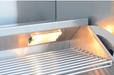 Close-up of a grill's interior light illuminating stainless steel cooking grates, enhancing visibility for nighttime or low-light grilling