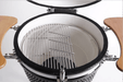 Close up view of open ceramic grill interior showing stainless steel cooking grates, hinged section for fuel addition, and folding wooden side shelves