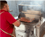 Man grilling meat on a stainless steel built-in charcoal grill with the lid open, showcasing spacious cooking area and outdoor kitchen setup