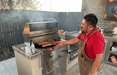 Man grilling ribs on a stainless steel built-in charcoal grill in a modern outdoor kitchen, showcasing a spacious cooking area and countertop