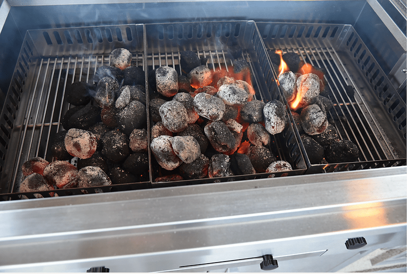 Lit charcoal briquettes inside a stainless steel charcoal grill, showcasing the even heat distribution and ventilation system for precise cooking