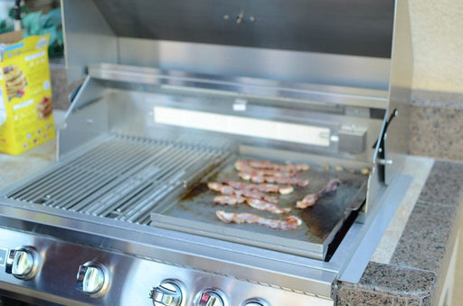 Stainless steel grill with a griddle plate cooking bacon, showcasing a spacious grilling surface and built-in burners in an outdoor setup