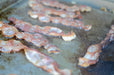 Close-up of crispy bacon strips sizzling on a flat stainless steel griddle, showing even cooking and grease pooling for easy cleanup