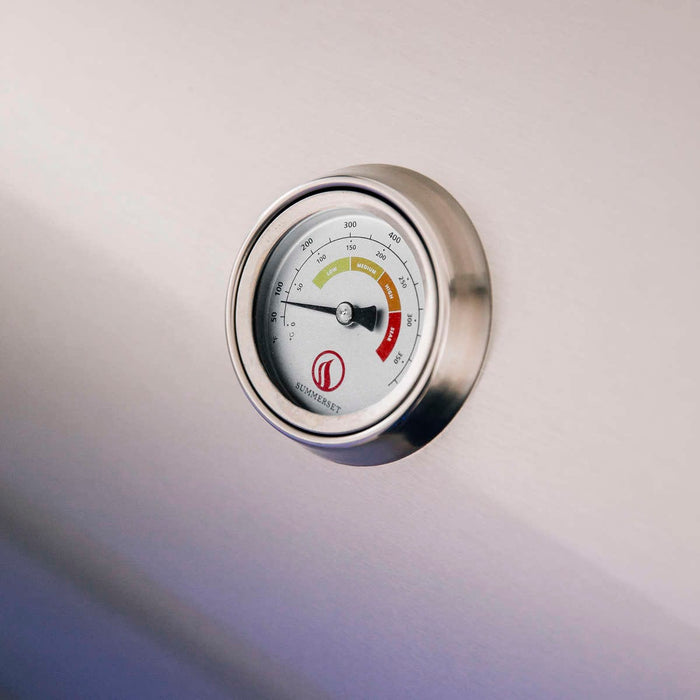 Close-up of a round temperature gauge on a stainless steel surface, showing temperature zones marked in green, yellow, and red.