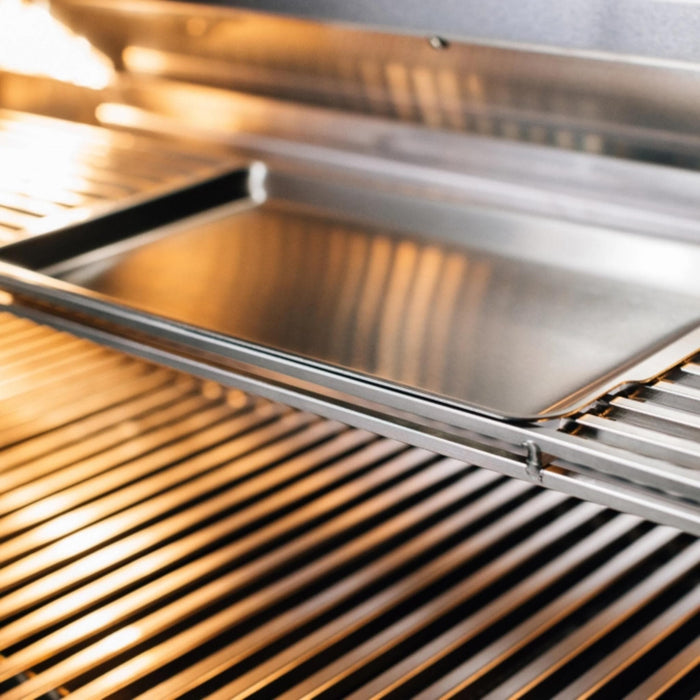 Close-up of TrueFlame built-in gas grill stainless steel cooking grates and removable cooking tray under illuminated interior lighting.